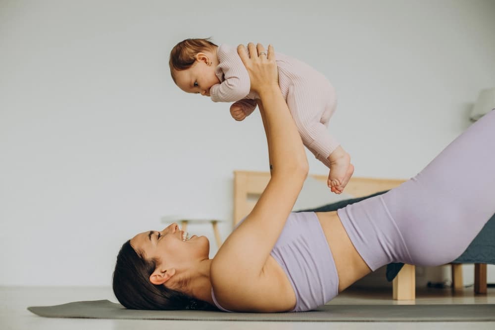 A mother on a yoga mat holding her baby up in the air.