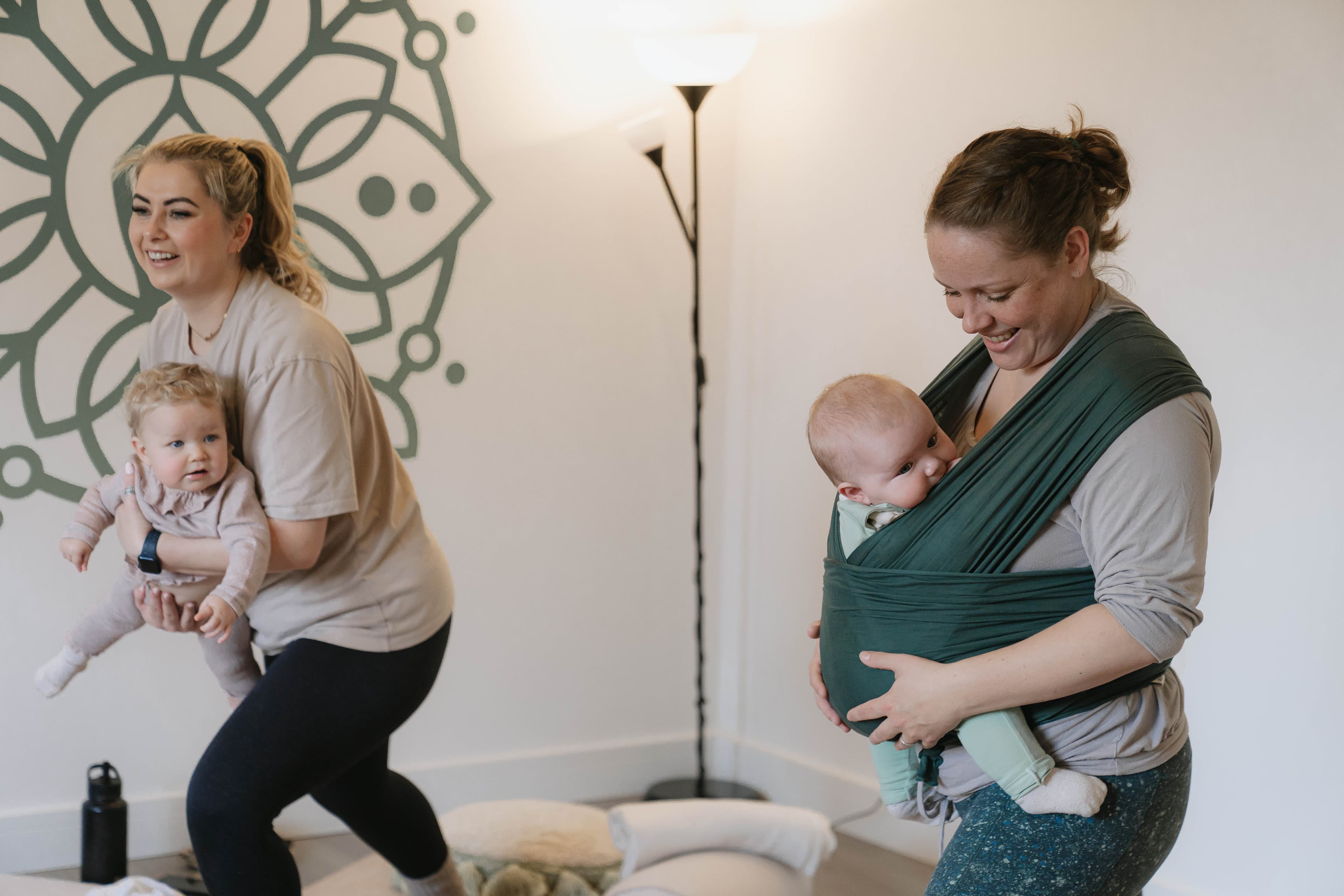 A mother on a yoga mat holding her baby up in the air.
