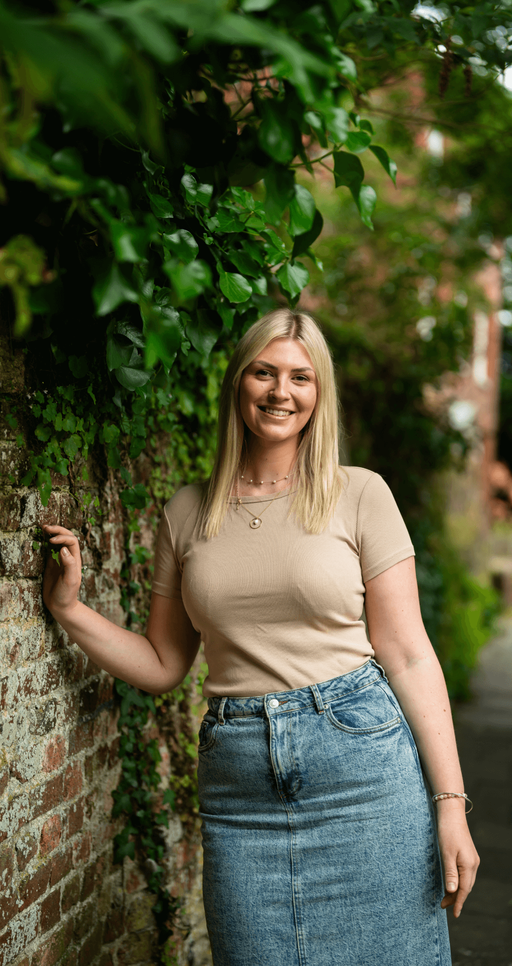 Rosie smiling beside a wall and greenery.