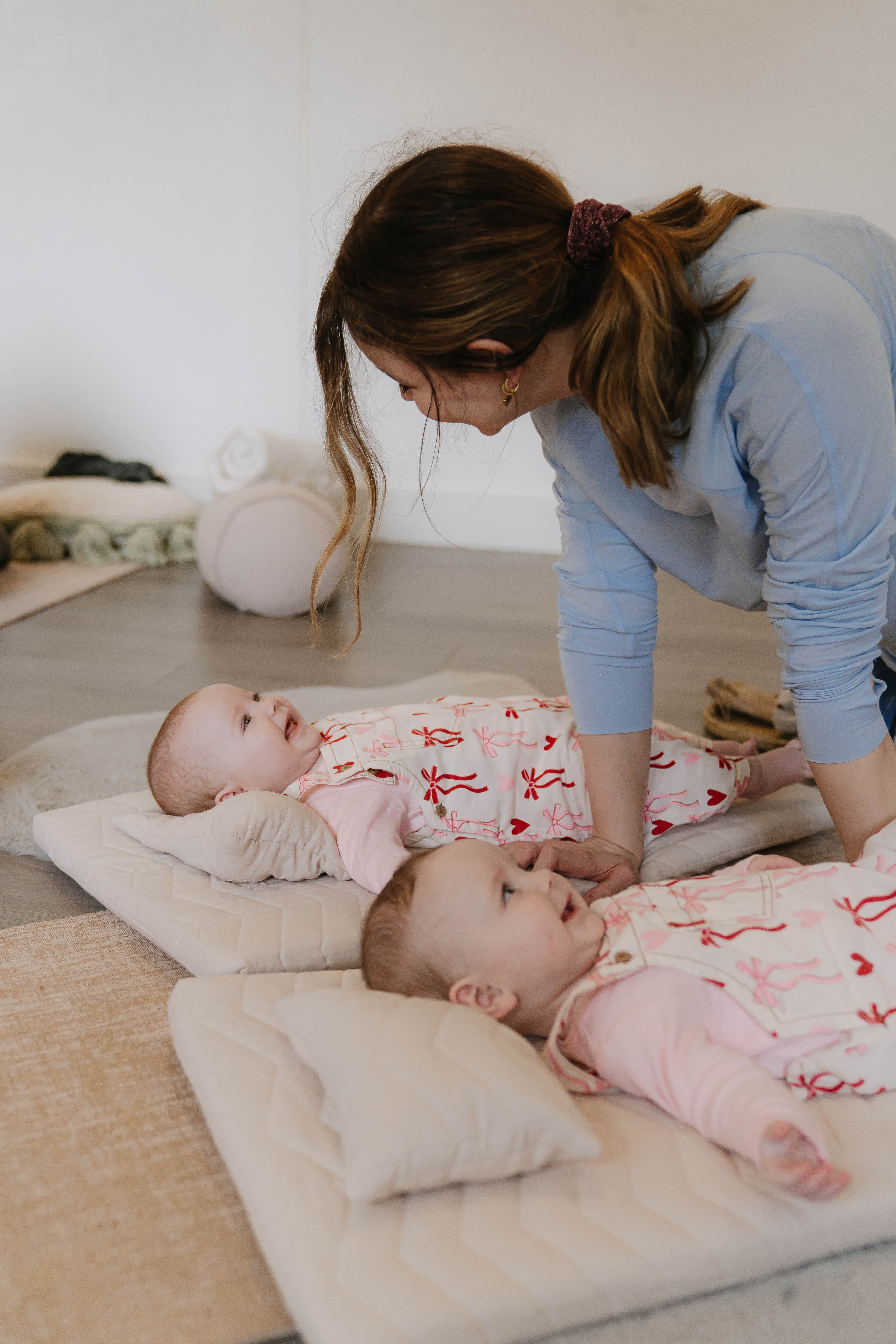 A mother smiling at her baby while laid on a yoga mat.