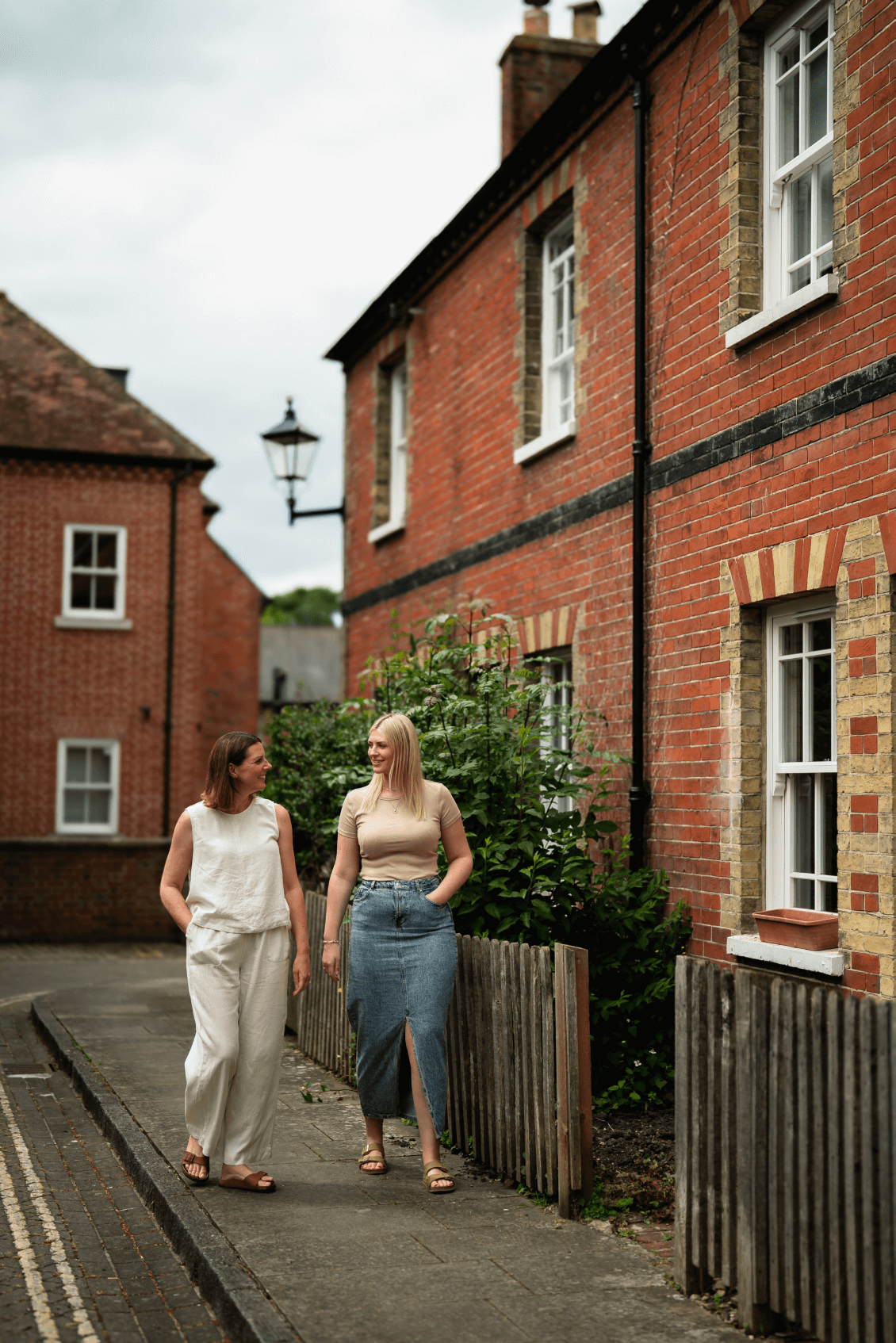 Tiffany and Rosie walking down a pavement with a house next to them.